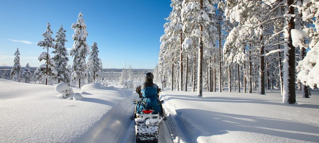 Sunny winter landscape with a man traveling Finnish Lapland with snowmobile